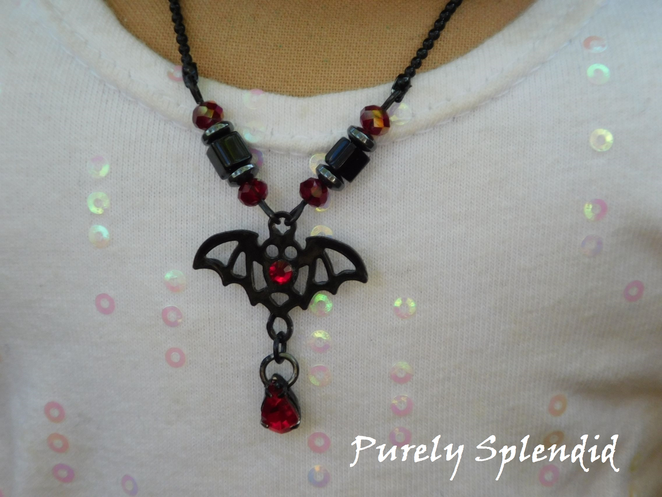 black bat necklace with red accents shown on an 18 inch doll