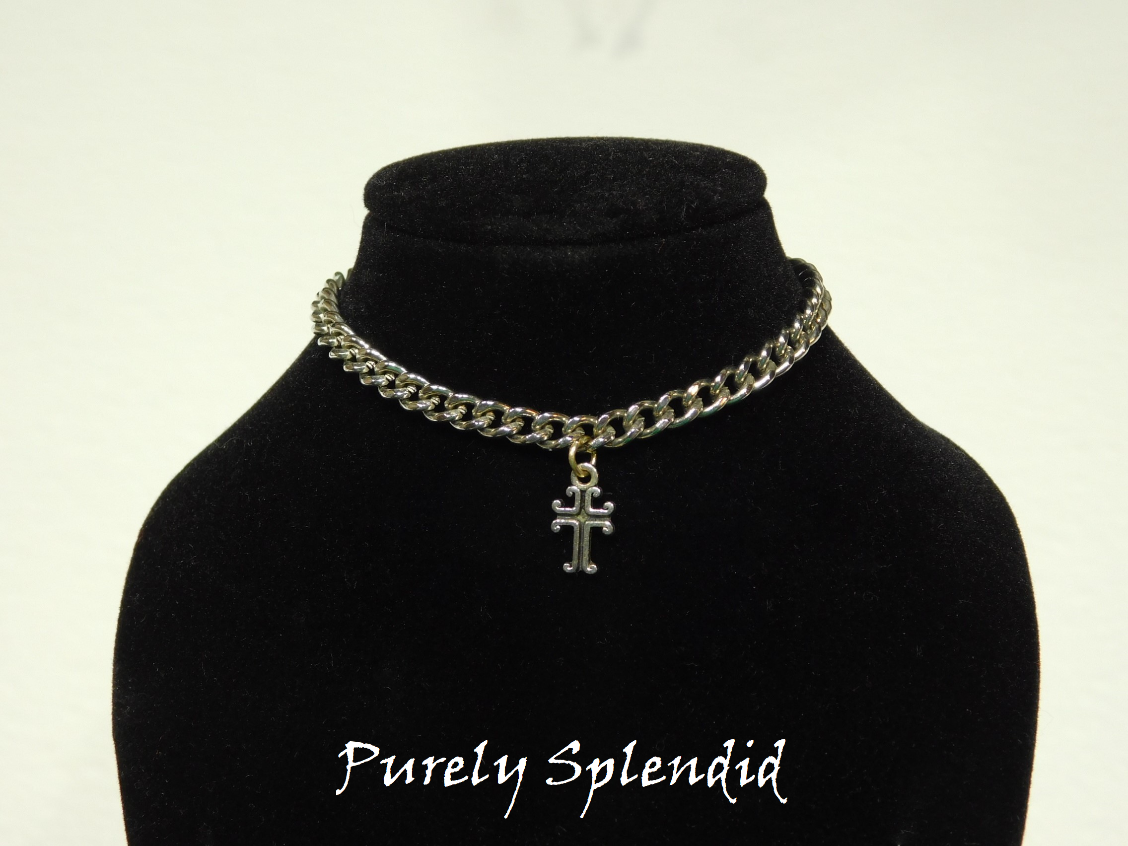 heavy silver chain with a cross charm hanging from shown on a doll mannequin