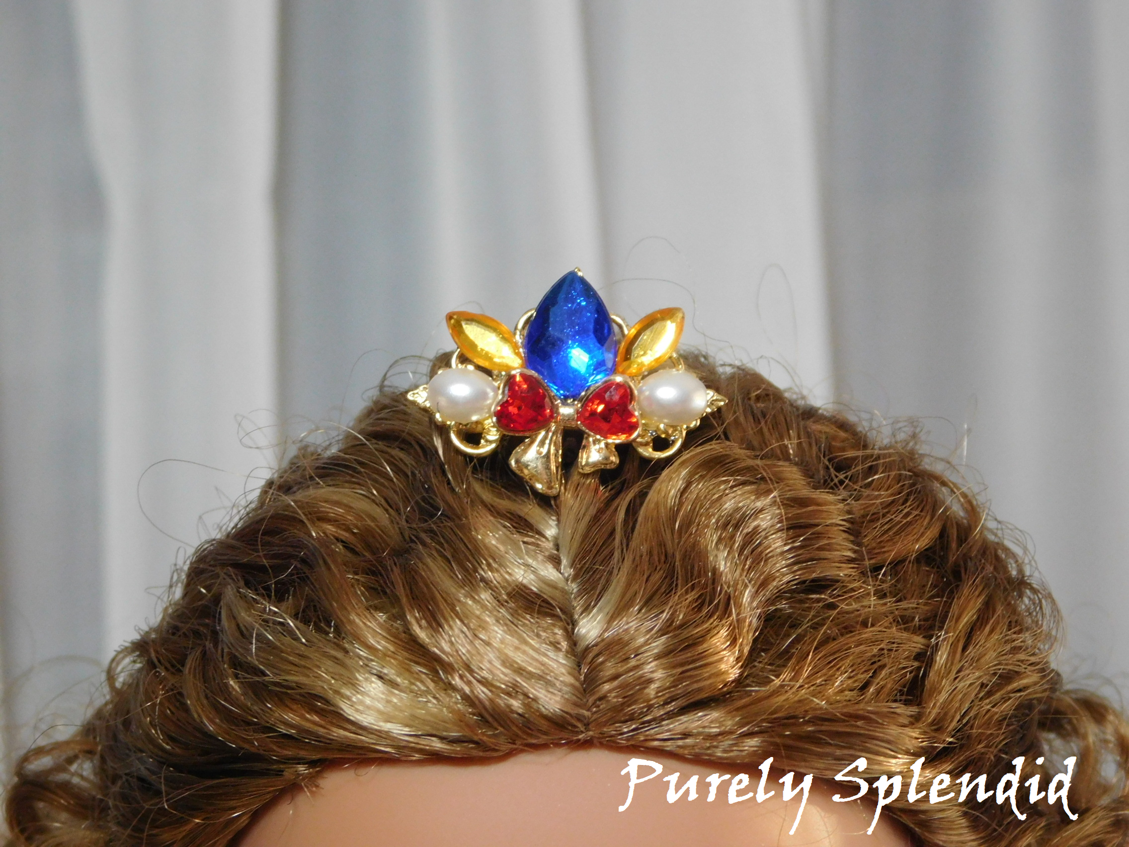 Snow White Crown worn by an 18 inch doll with a large blue center stone, sparkling red bow with white pearls on either side of it