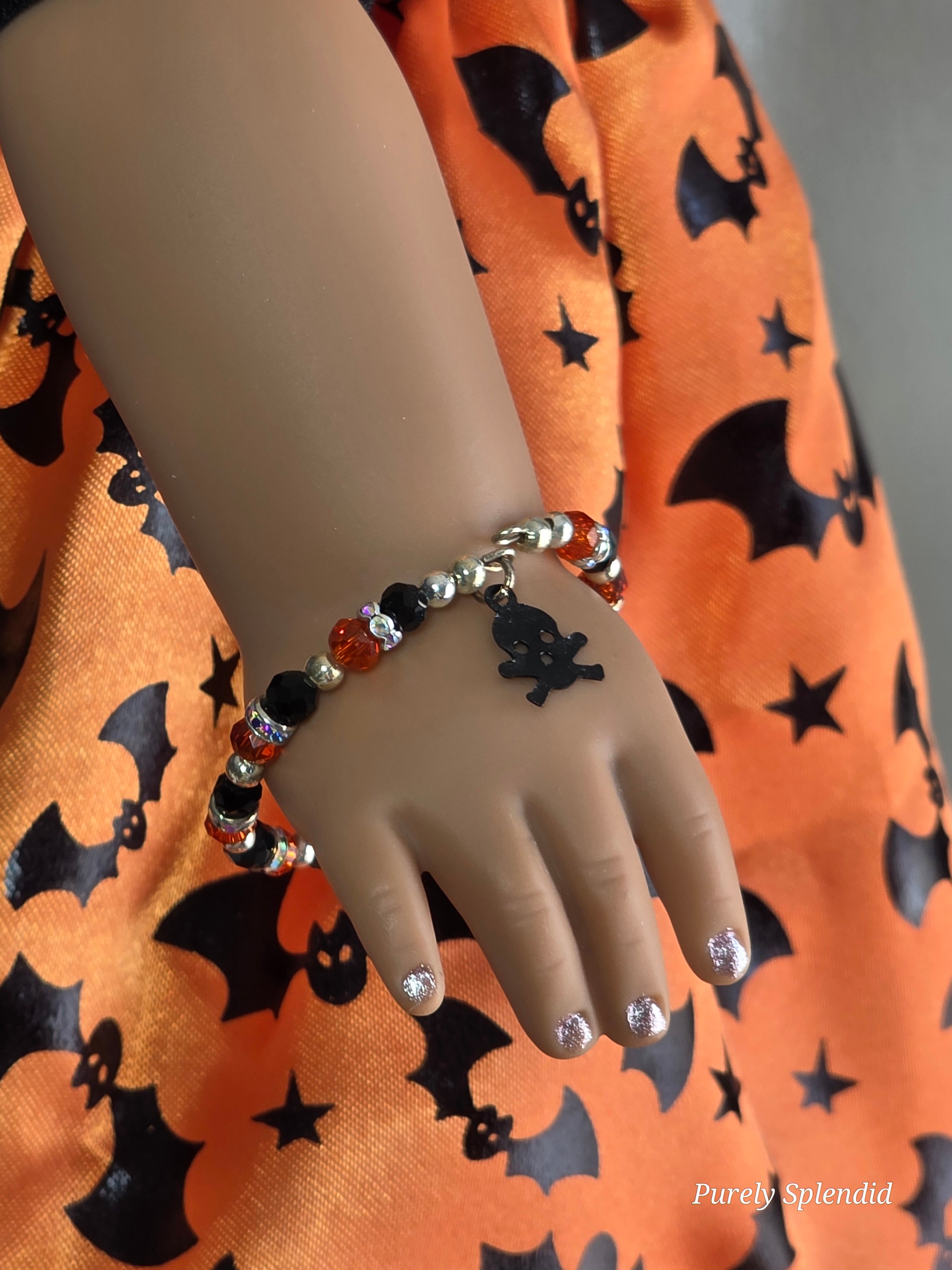 Sparkling orange and black crystal bracelet with black skull and crossbones charm worn by an 18 inch doll