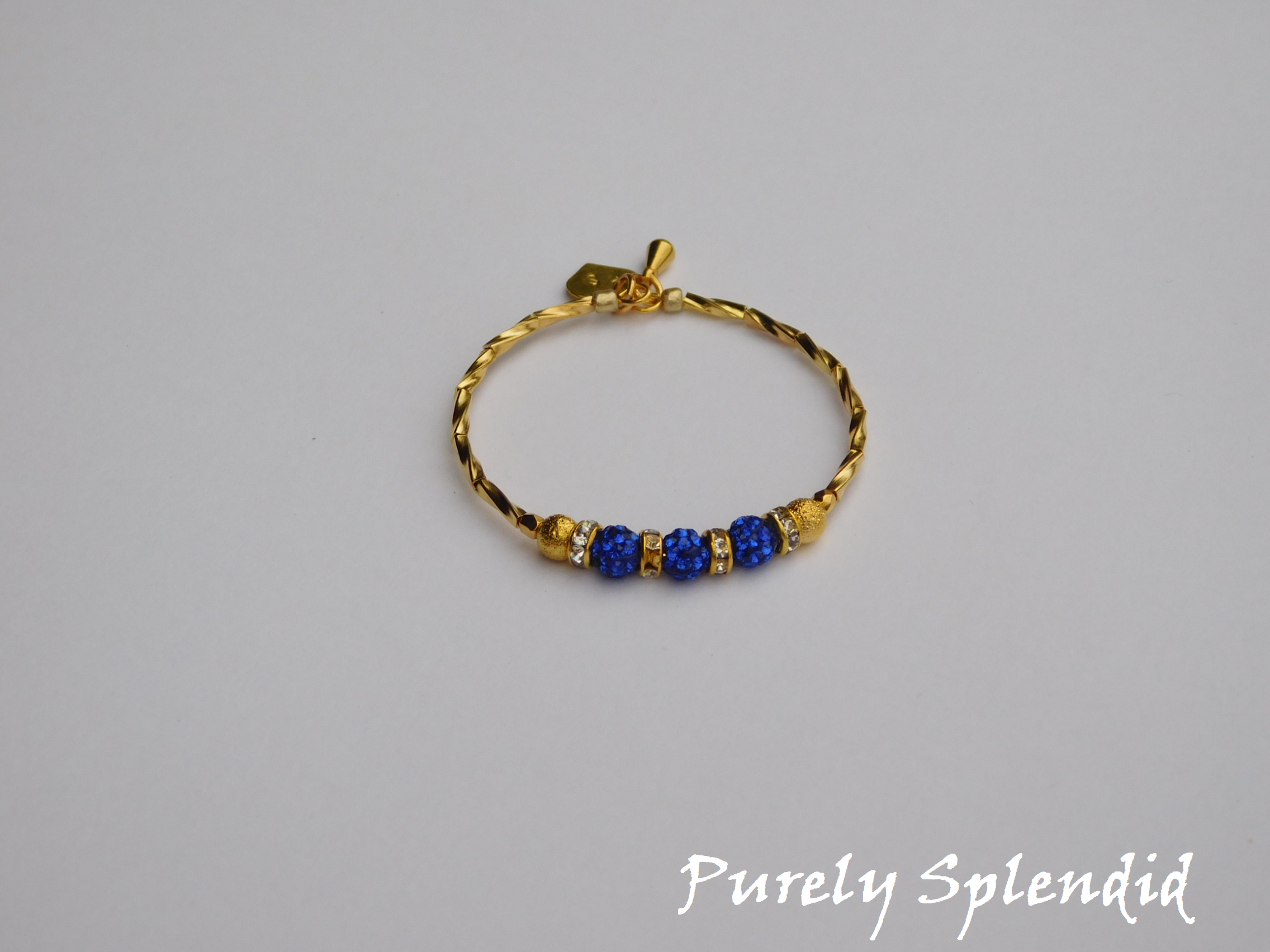 Gold bracelet with three round sparkling blue beads each surrounded with a ring of sparkle