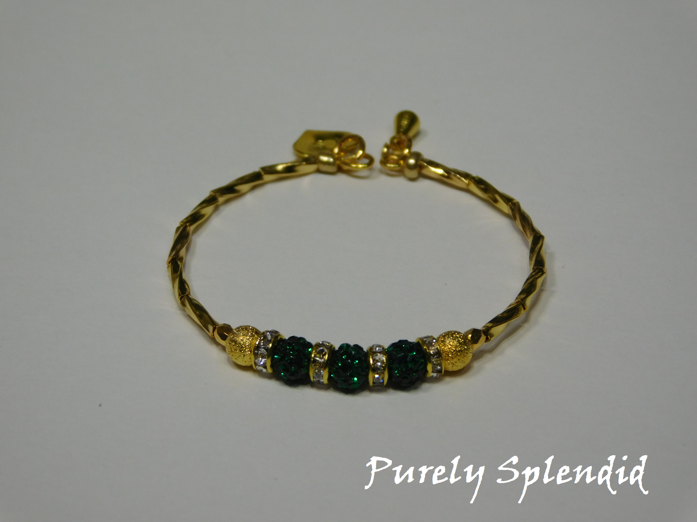 Gold bracelet with three round sparkling green beads each surrounded with a ring of sparkle