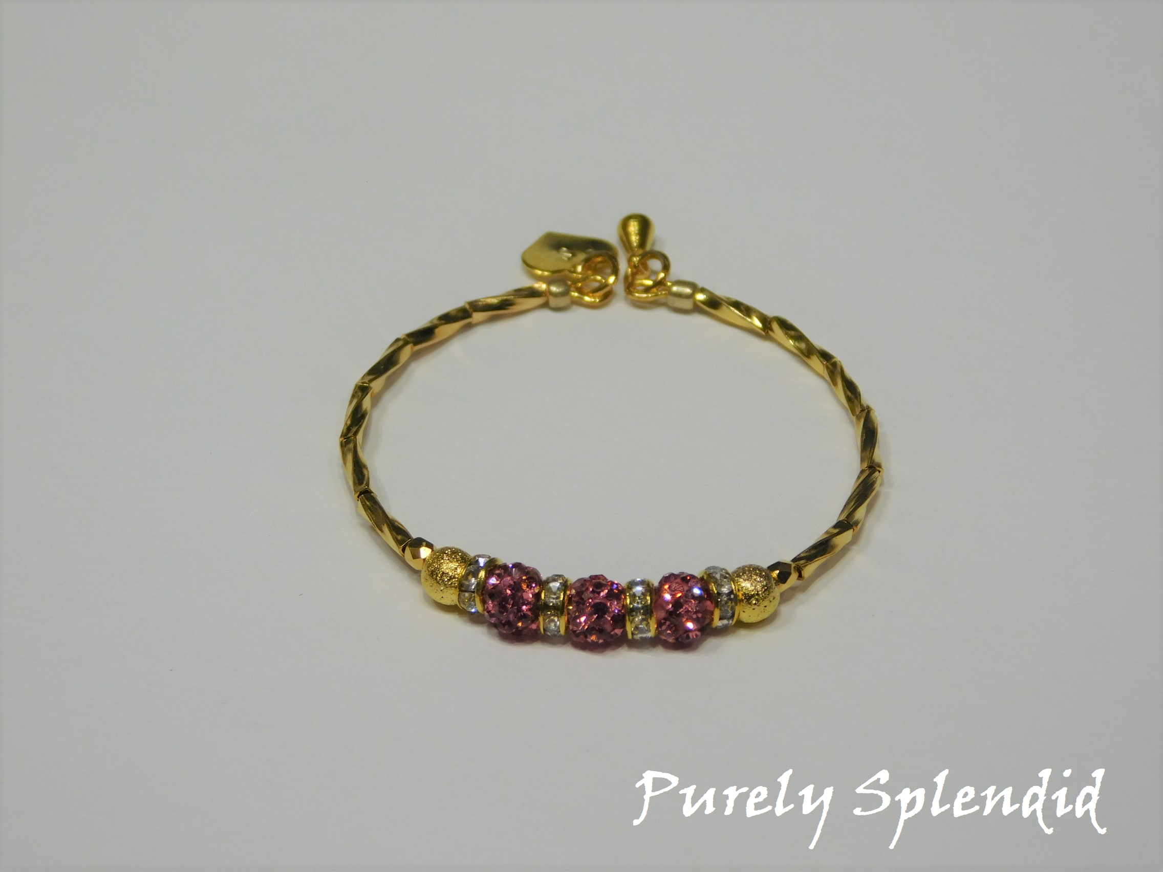 Gold bracelet with three round sparkling pink beads each surrounded with a ring of sparkle