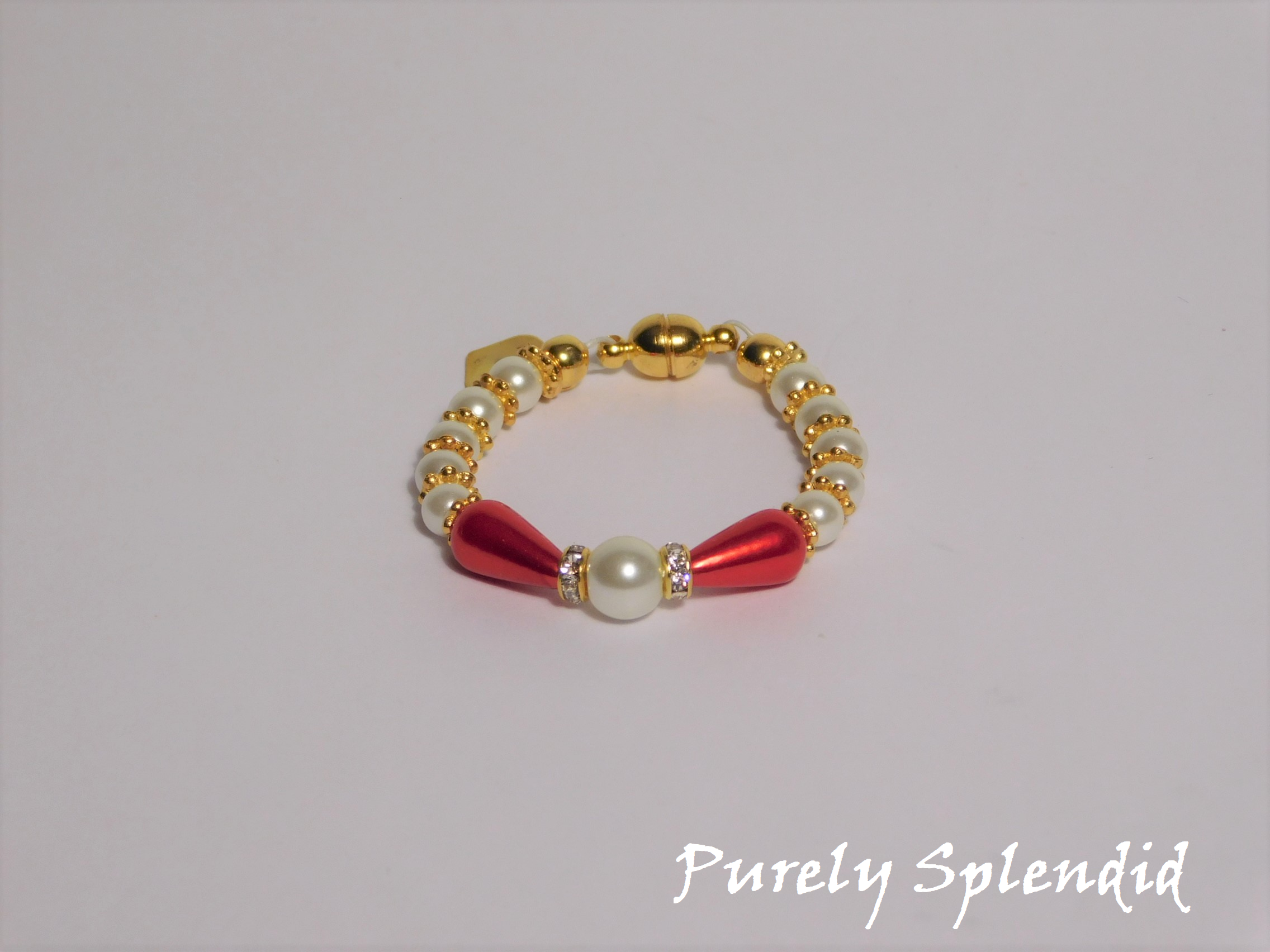 round white pearls with gold spacer beads with the main focus made up of one large white pearl bead surrounded by a thin sparkling bead and red pear shaped pearl