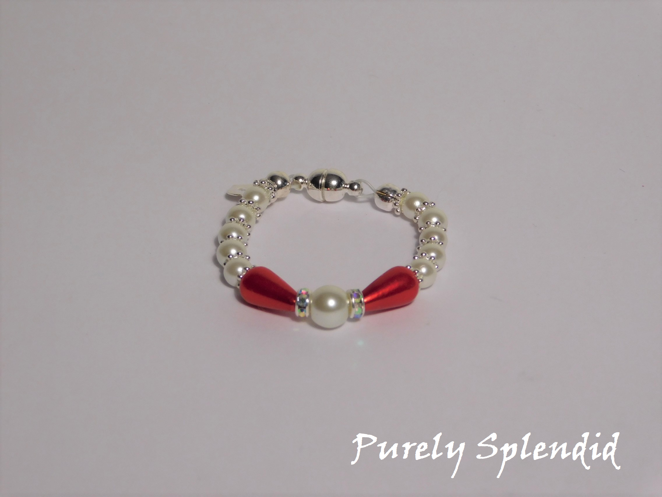 round white pearls with silver spacer beads with the main focus made up of one large white pearl bead surrounded by a thin sparkling bead and red pear shaped pearl