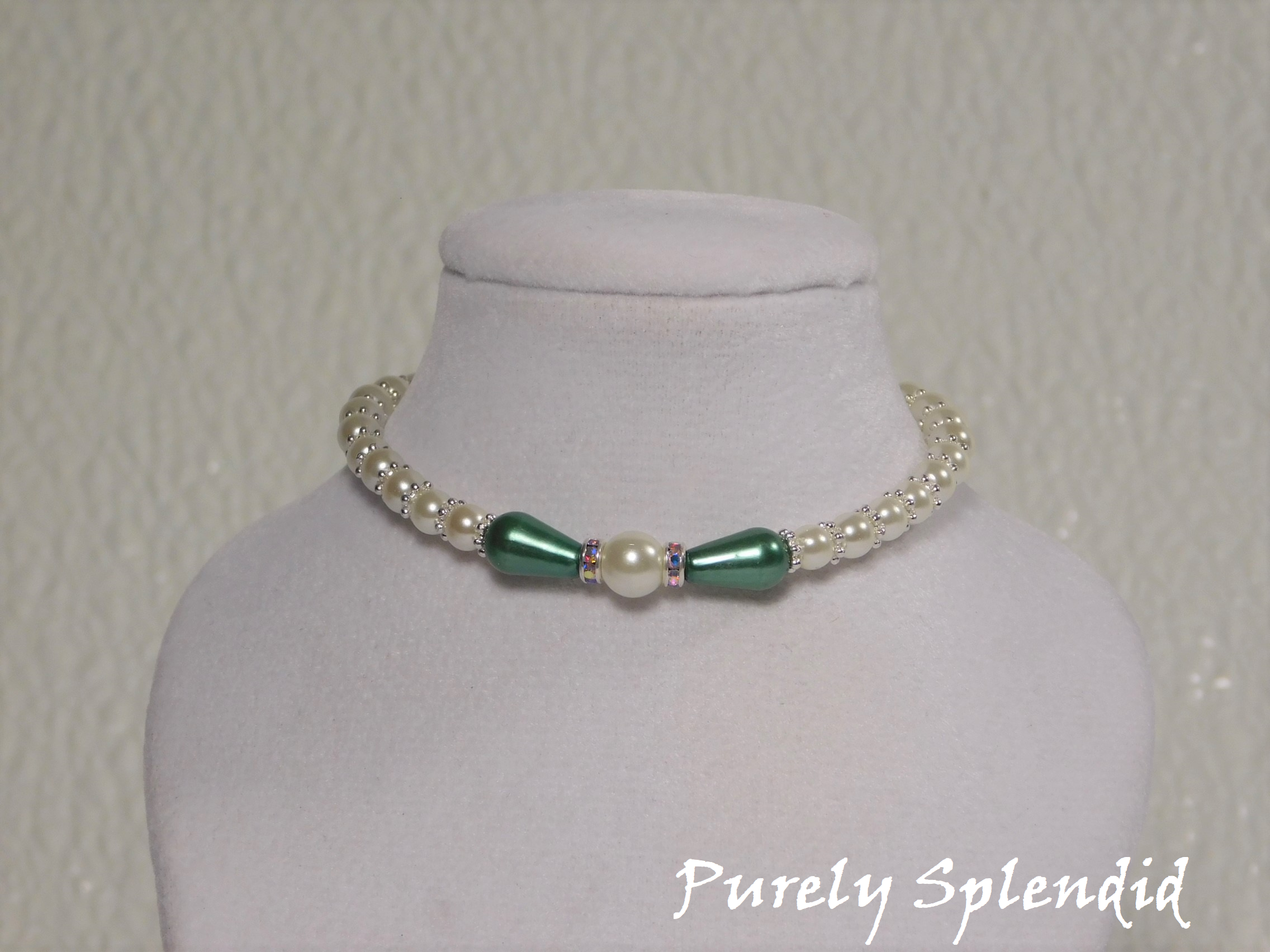 one large round white pearl surrounded by a thin sparkling bead and green pear shaped pearl bead. The rest of the necklace is made up with round white pearls alternating with silver spacer beads