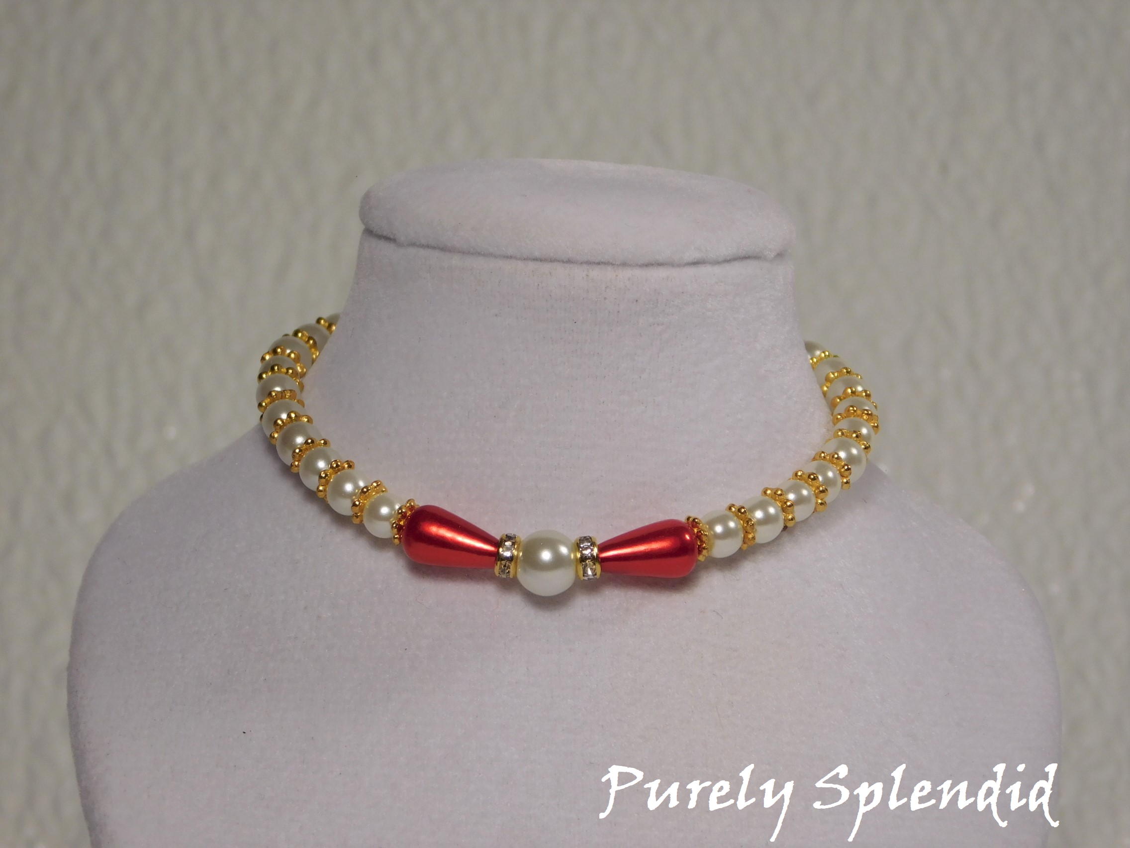 one large round white pearl surrounded by a thin sparkling bead and red pear shaped pearl bead. The rest of the necklace is made up with round white pearls alternating with gold spacer beads
