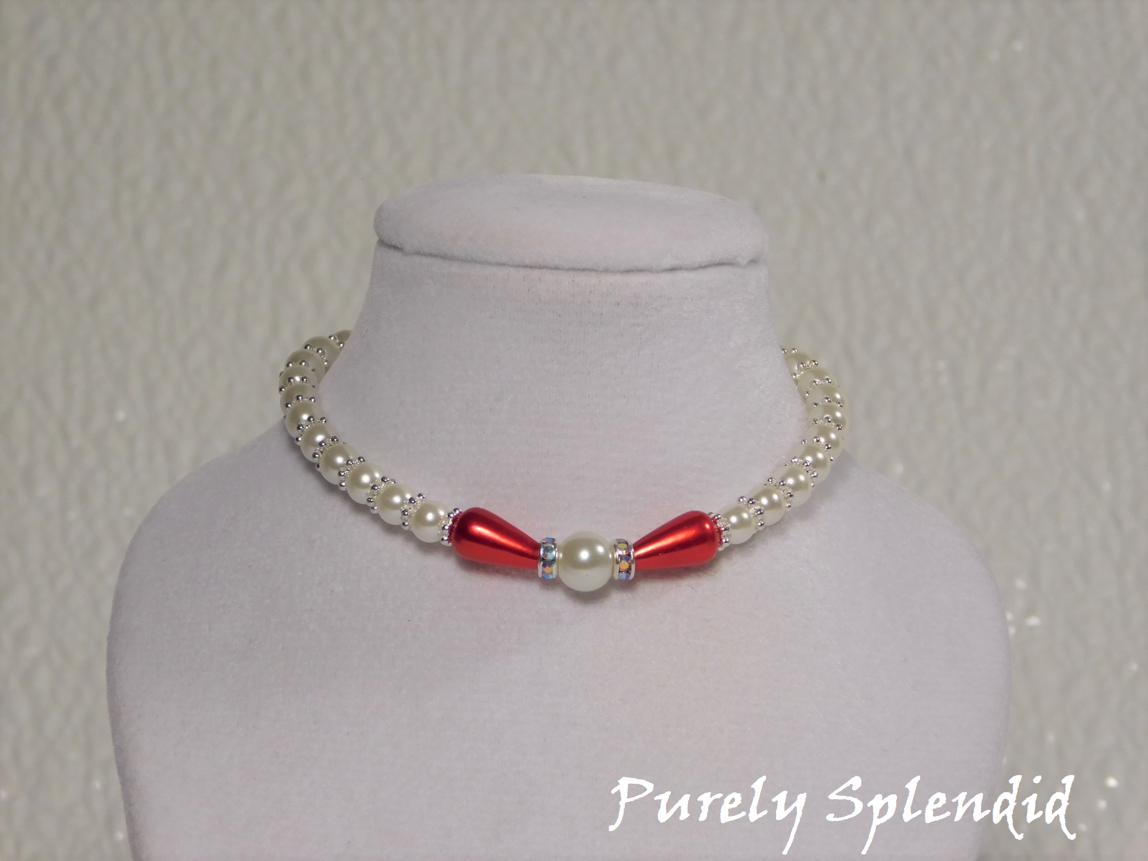 one large round white pearl surrounded by a thin sparkling bead and red pear shaped pearl bead. The rest of the necklace is made up with round white pearls alternating with silver spacer beads
