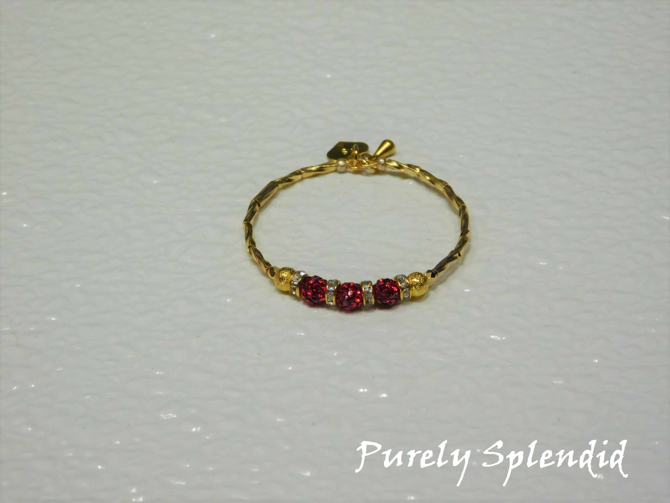 Gold bracelet with three round sparkling red beads each surrounded with a ring of sparkle