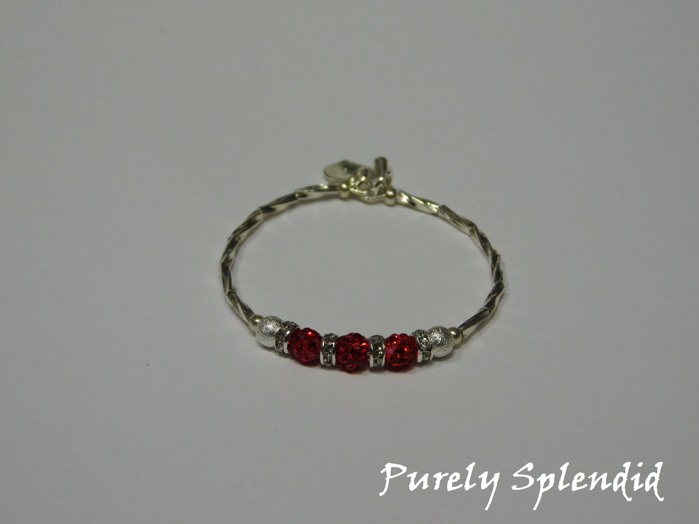 Silver bracelet with three round sparkling red beads each surrounded with a ring of sparkle