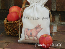 Load image into Gallery viewer, close up picture of a vintage style pink pig fabric bag with the words ...this little piggy. Bag is cinched up sitting in front of a basket of apples
