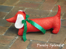 Load image into Gallery viewer, dachshund made with red fabric with gold dots, light beige ears and under body wearing a sparkling green bow around the neck and a silver heart dangling from it
