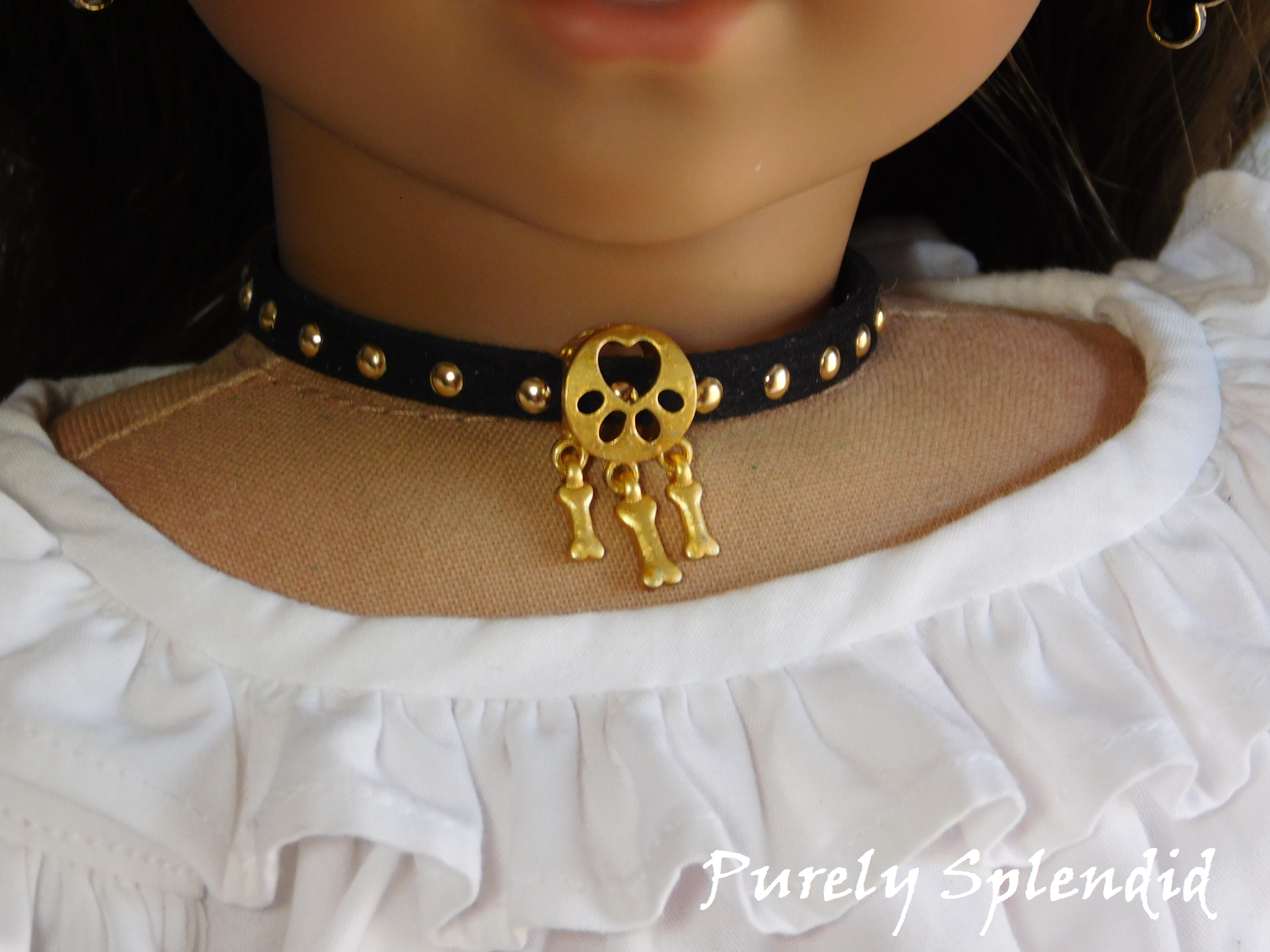 black choker with gold dots and a gold dog bone charm worn by an 18 inch doll