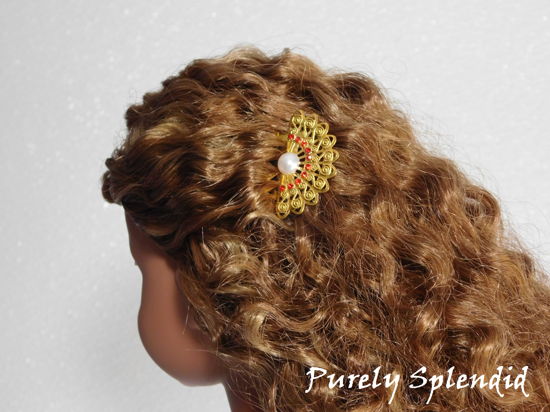 doll wearing a gold filigree fan with red rhinestones and a pearl center hair comb