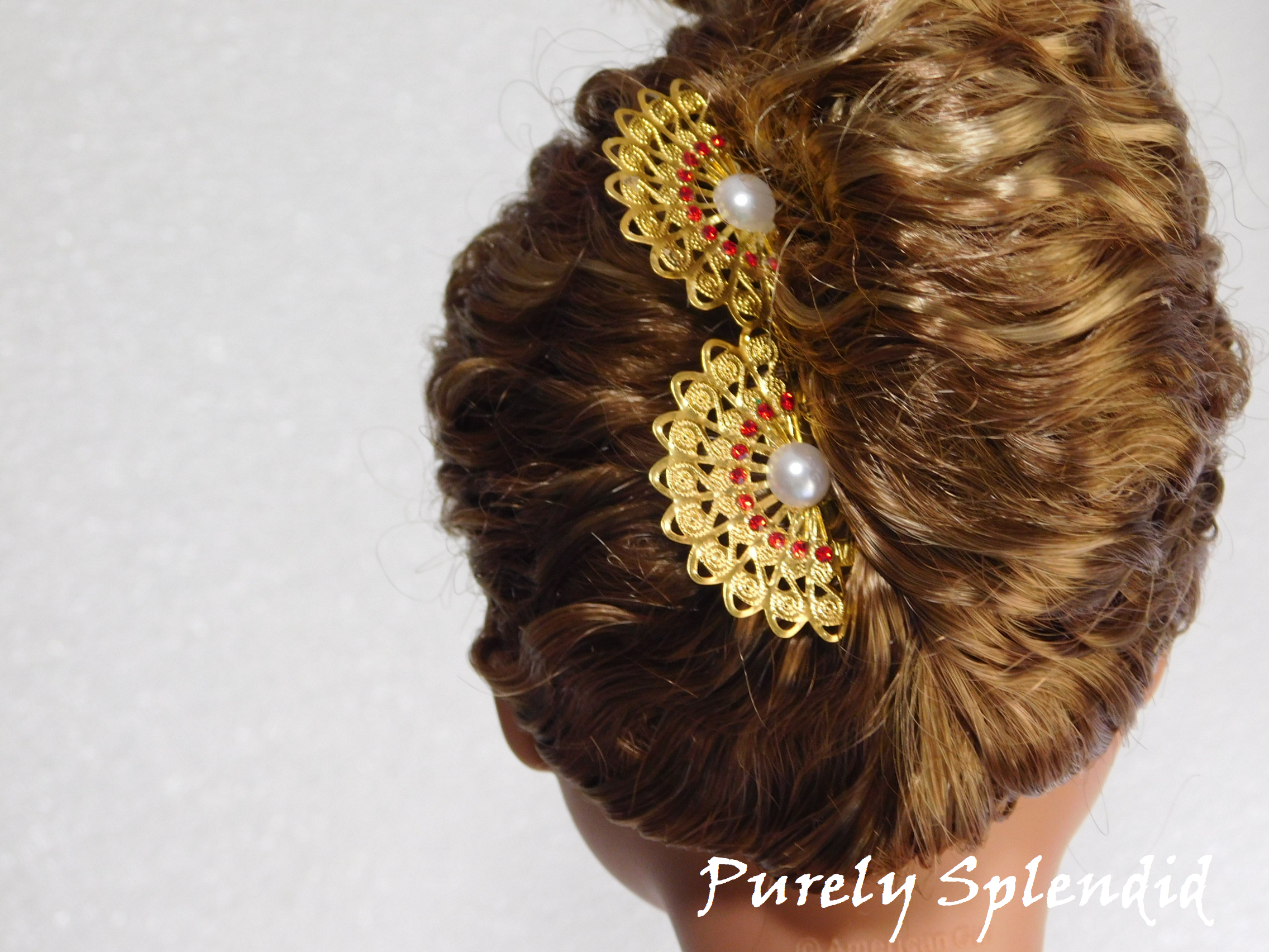 set of two gold filigree fans with red rhinestones and a pearl center shown in an 18 inch dolls updo