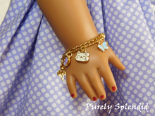 Load image into Gallery viewer, 18 inch doll shown wearing a Happy Charm Bracelet with a white happy cat face, blue butterfly and purple heart charm

