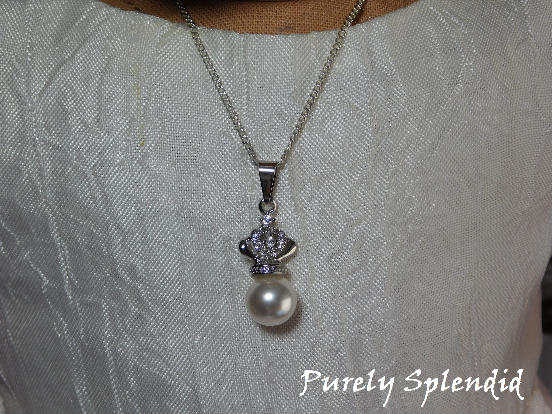 Large white pearl topped with a sparkling silver crown hanging from a fine silver chain