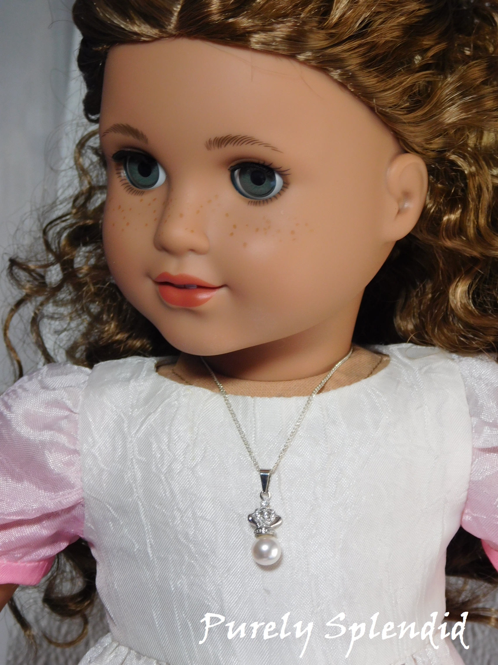 18 inch doll wearing a large white pearl topped with a sparkling silver crown hanging from a fine silver chain necklace