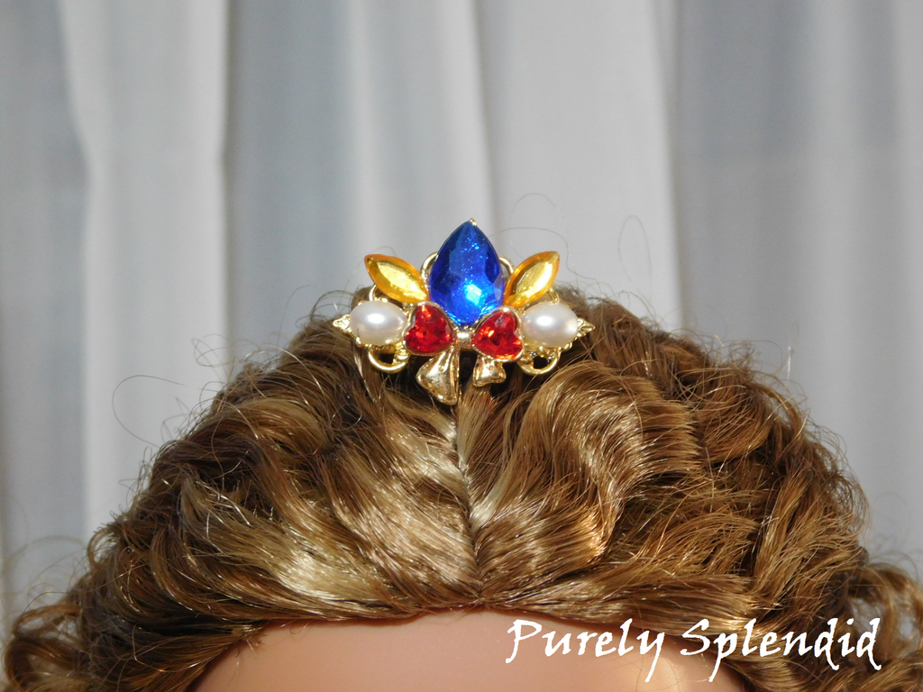 Snow White Crown worn by an 18 inch doll with a large blue center stone, sparkling red bow with white pearls on either side of it