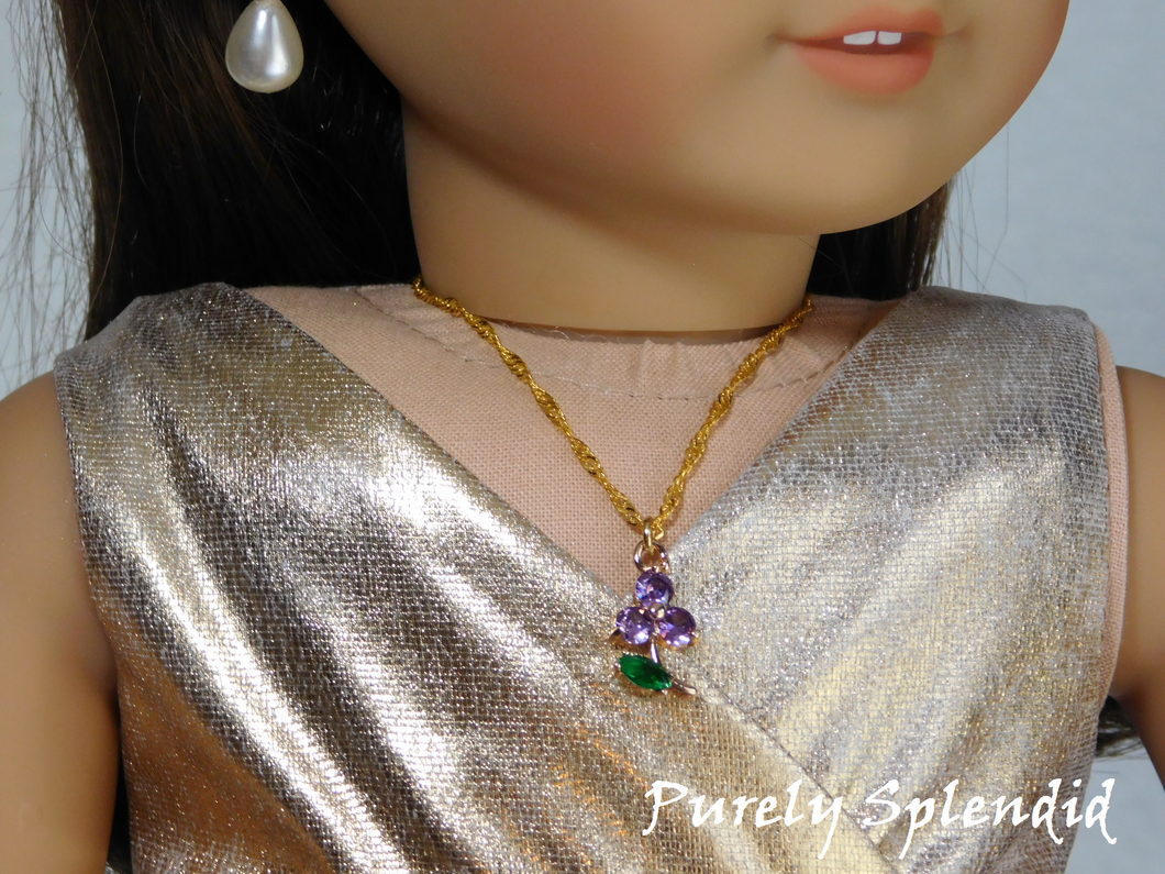 18 inch doll shown wearing a Sparkling Purple Flower Necklace. Flower charm has 3 sparkling purple petals and a sparkling green leaf hanging from a pretty twisted gold chain.