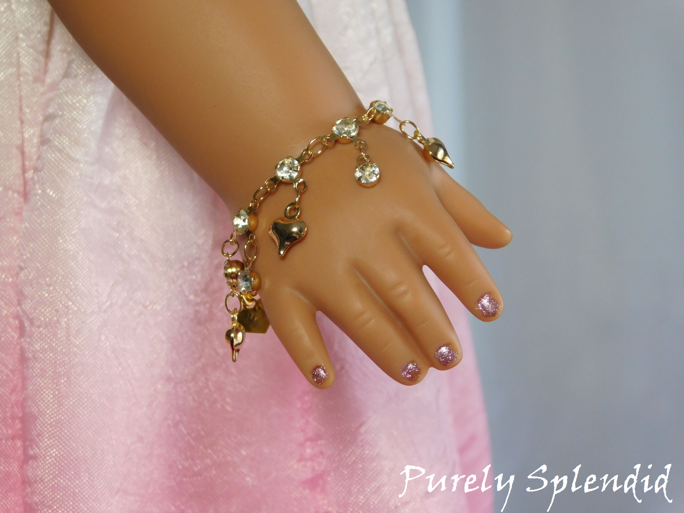 puffy gold heart charms and sparking rhinestone drops on a sparkling gold bracelet shown worn by an 18 inch doll