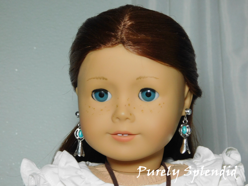 18 inch doll shown wearing a pair of Squash Blossom Earrings featuring an oval turquoise colored stone as a part of the silver blossom