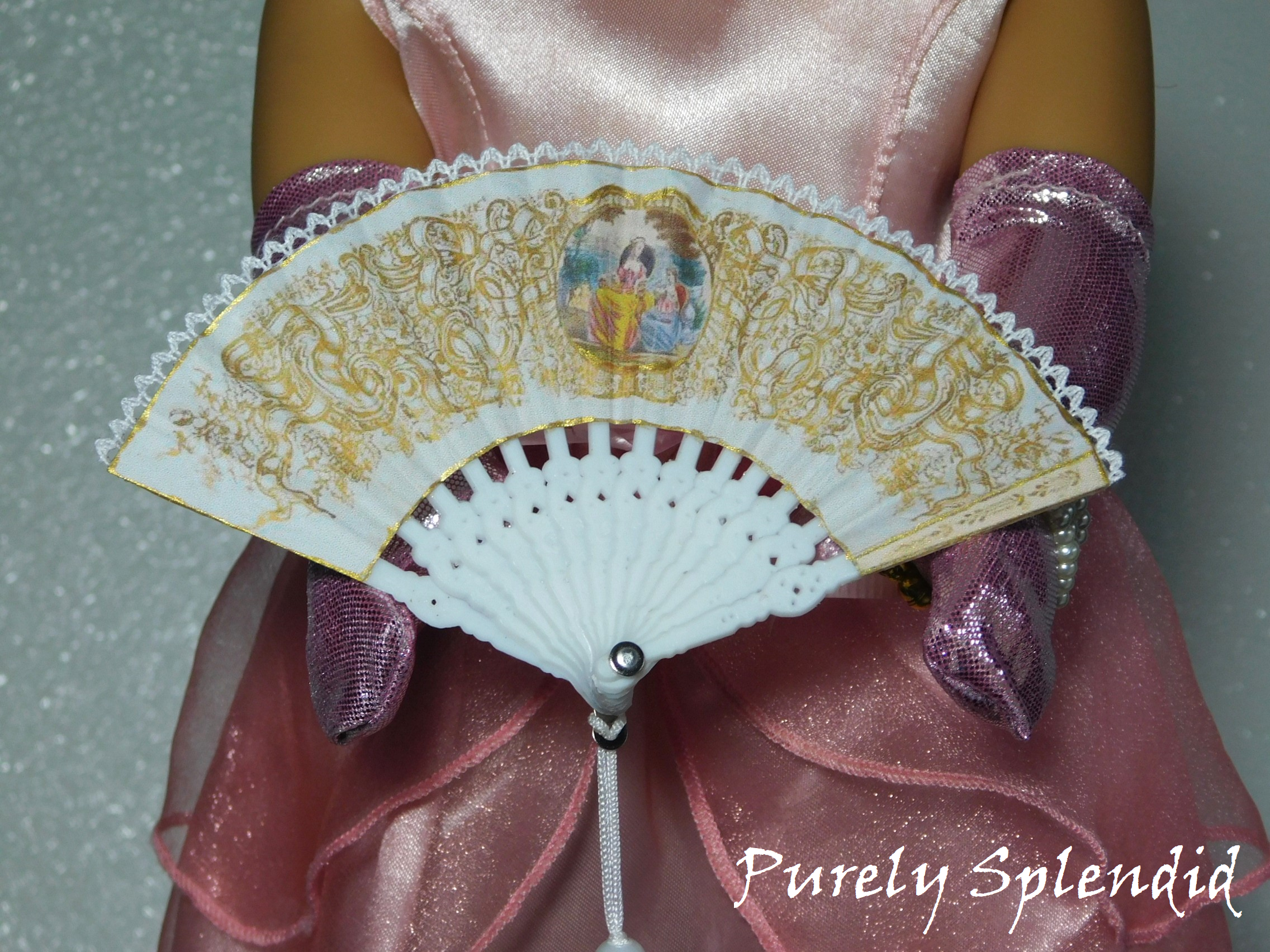Elegant White Hand Fan with a Victorian picture of ladies in the middle with gold scroll work surrounding them. Fan is edged in gold as well as white lace