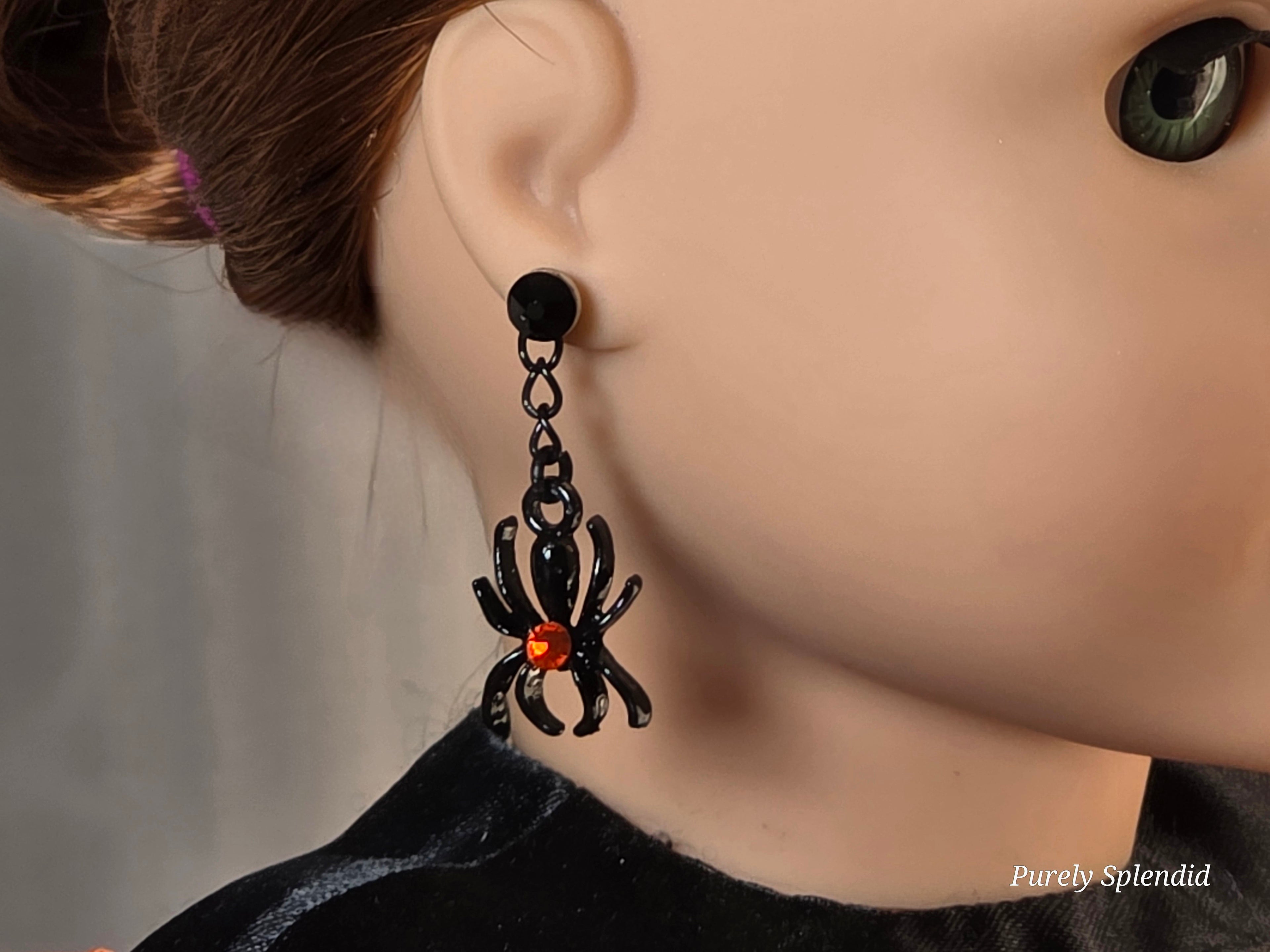 Black spider earrings with a sparkling red center worn by an 18 inch doll