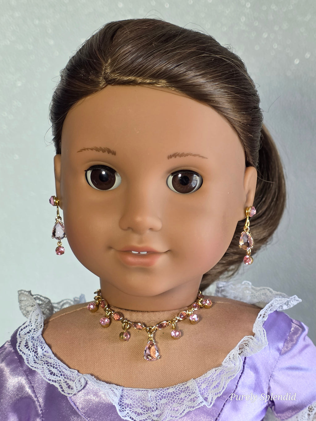 18 inch doll wearing pink necklace with pink dangles and matching earring dangles and studs