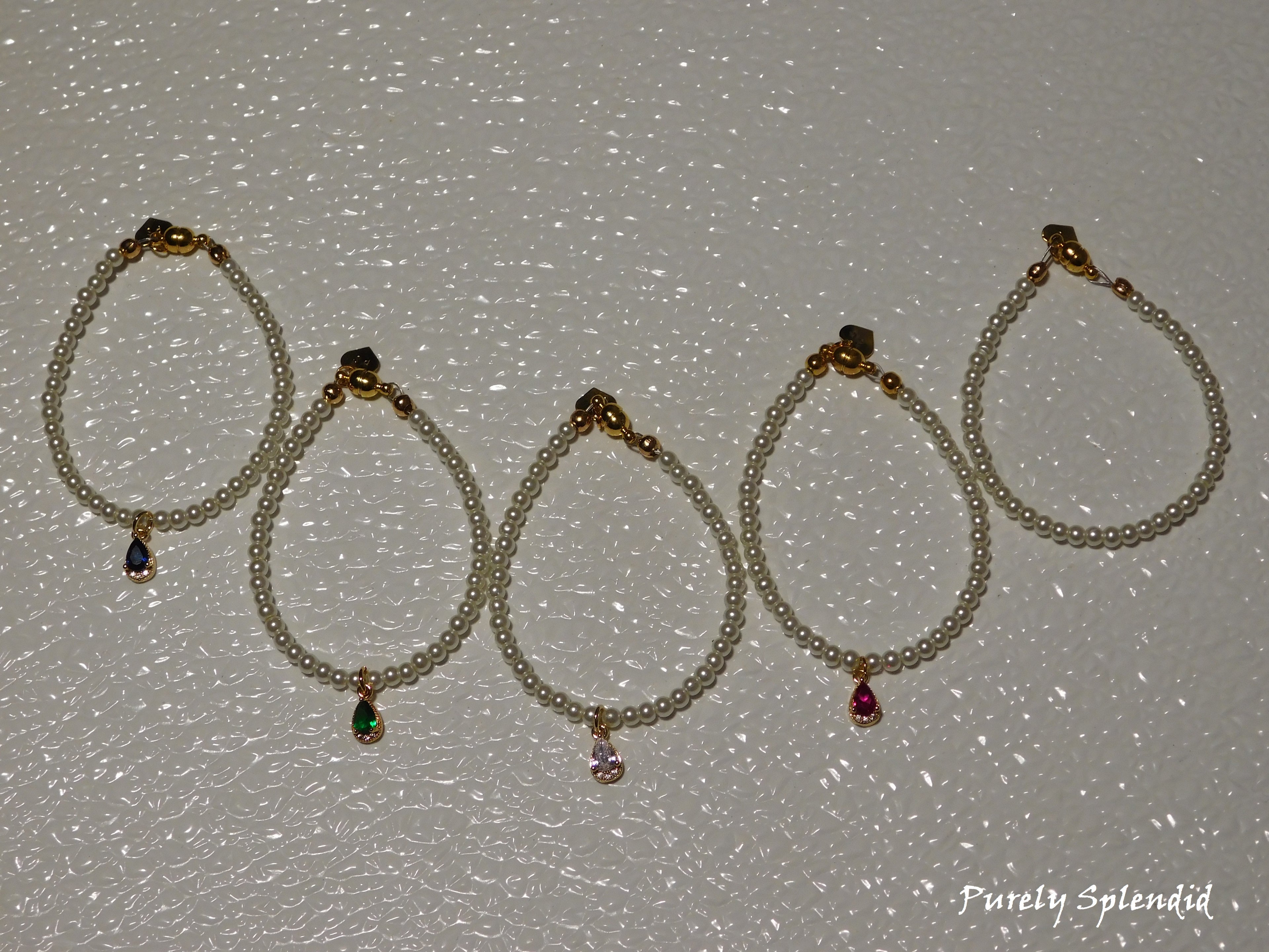 five Classic Pearl Necklaces one with a blue center pendant, one with a green, one with a clear one with a pink and the simple pearl stand without a pendant