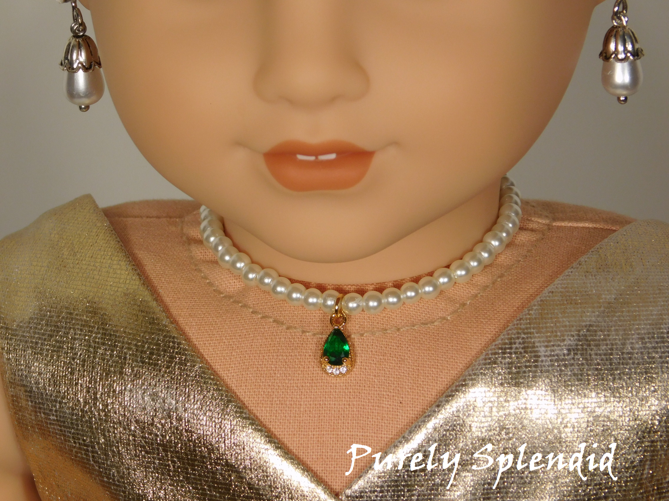 18 inch doll shown all dressed up wearing a string of white pearls with a sparkling green center pendant