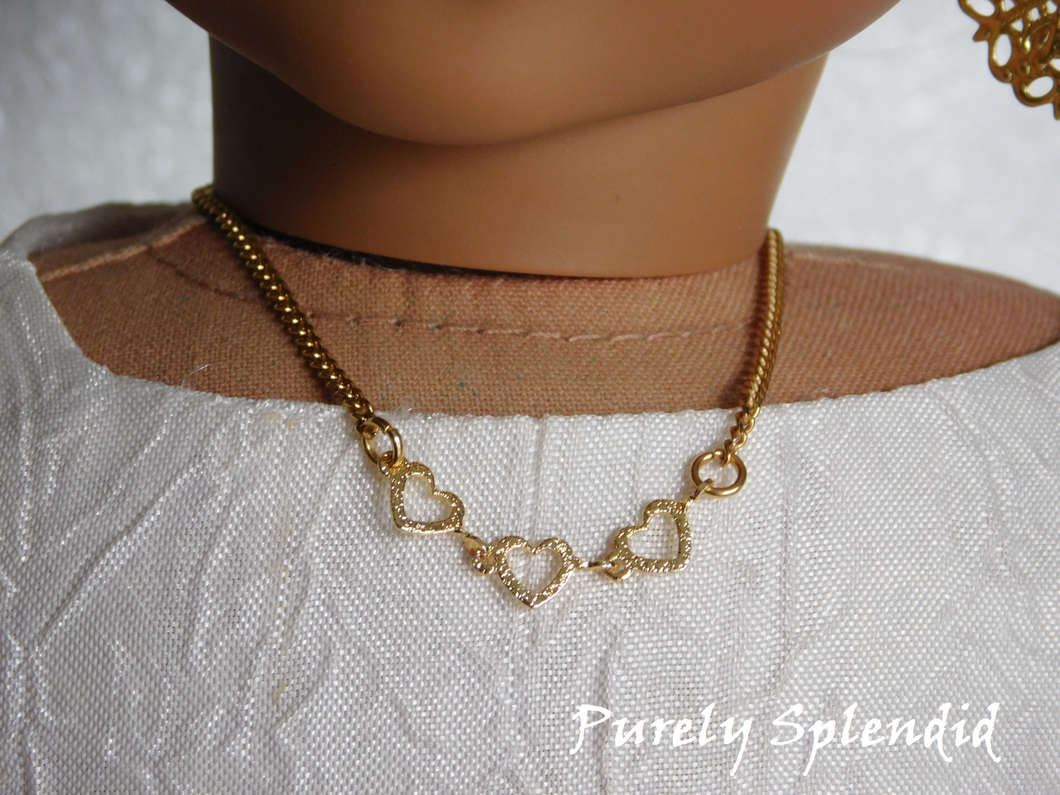 Three golden open hearts on a pretty chain make up this Dainty Gold Heart Necklace. Shown worn by an 18 inch doll
