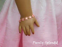 Load image into Gallery viewer, 18 in doll shown wearing a Dainty Pink Flower Bracelet made up of 10 small pink daisy like flowers
