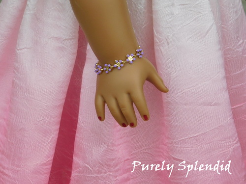 ten small purple daisy like flowers make up this Dainty Purple Flower Bracelet shown worn by an 18 inch doll