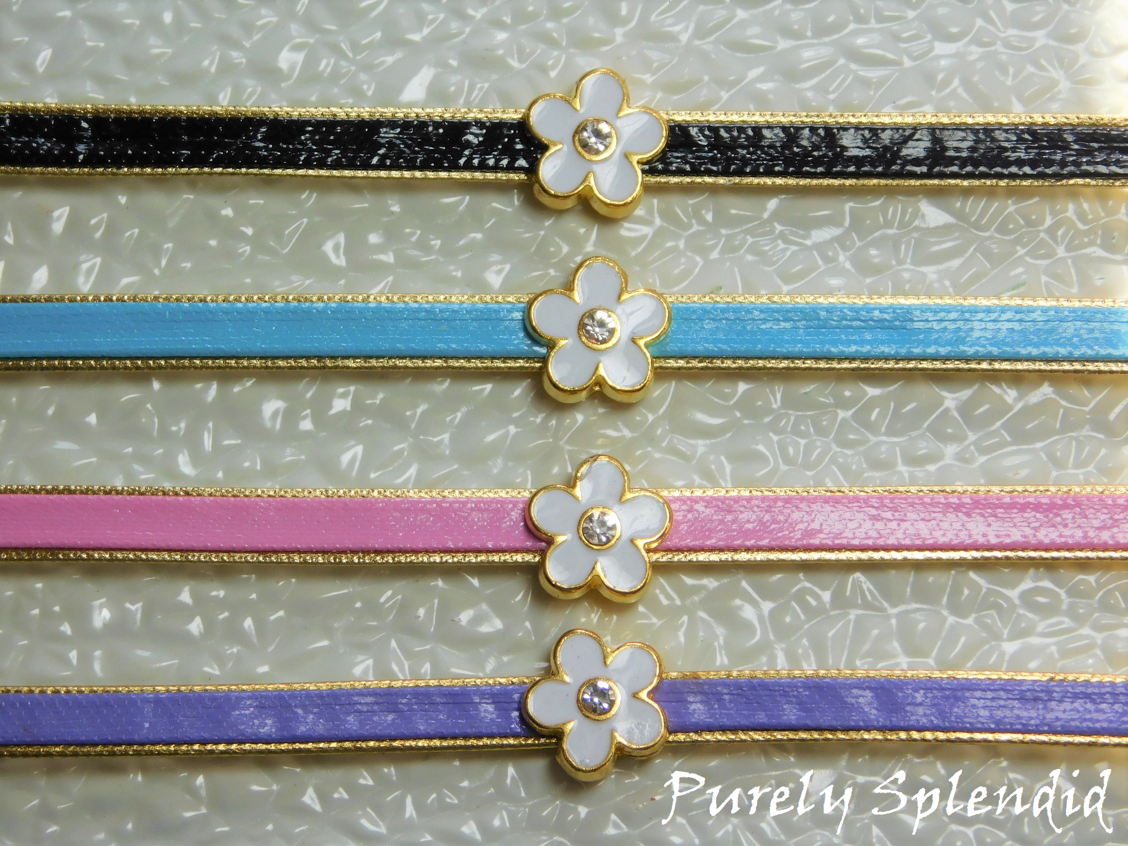Four pretty Flower Choker Necklaces on a white background - black, blue, pink and purple leather like choker with a gold rimmed white enamel flower with sparkling center