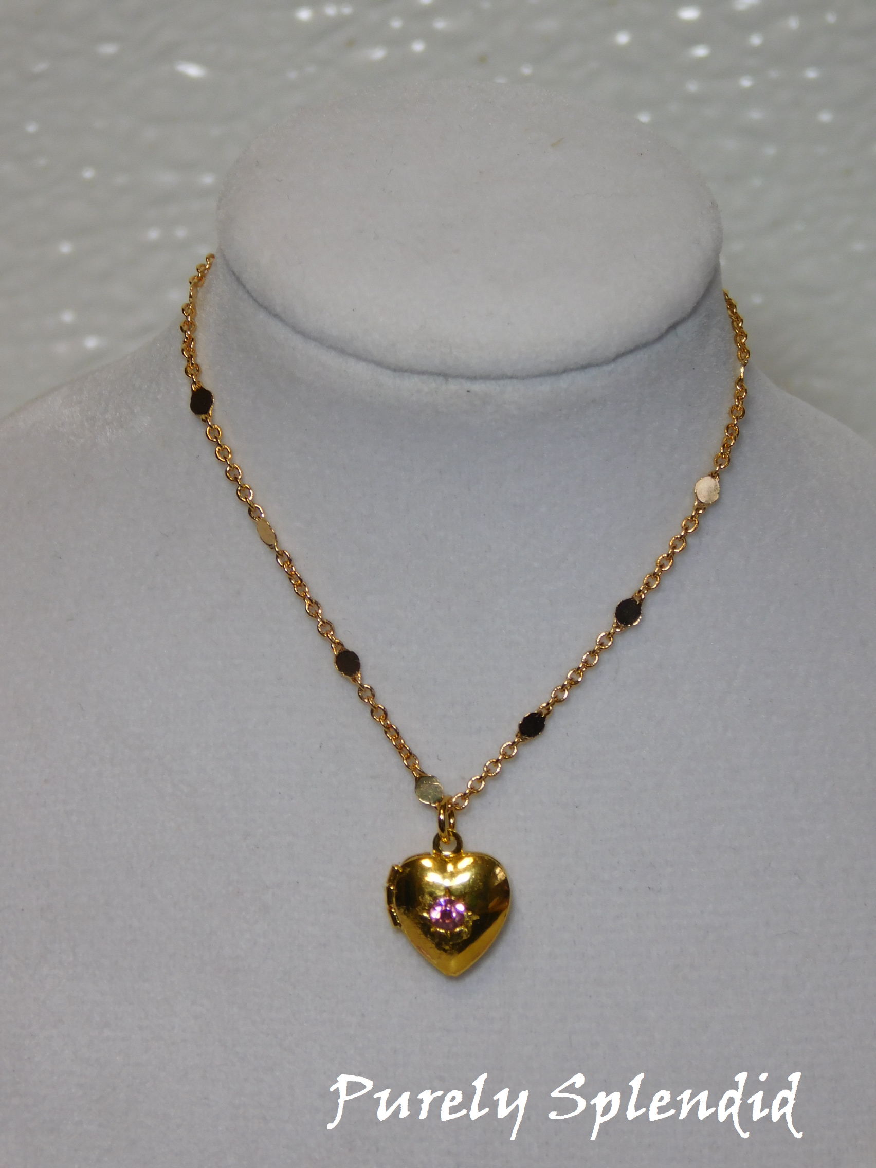 gold heart locket with a pink crystal in the center hanging on a pretty gold chain  