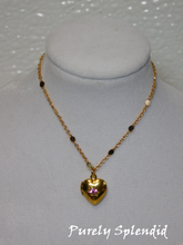 Load image into Gallery viewer, gold heart locket with a pink crystal in the center hanging on a pretty gold chain  
