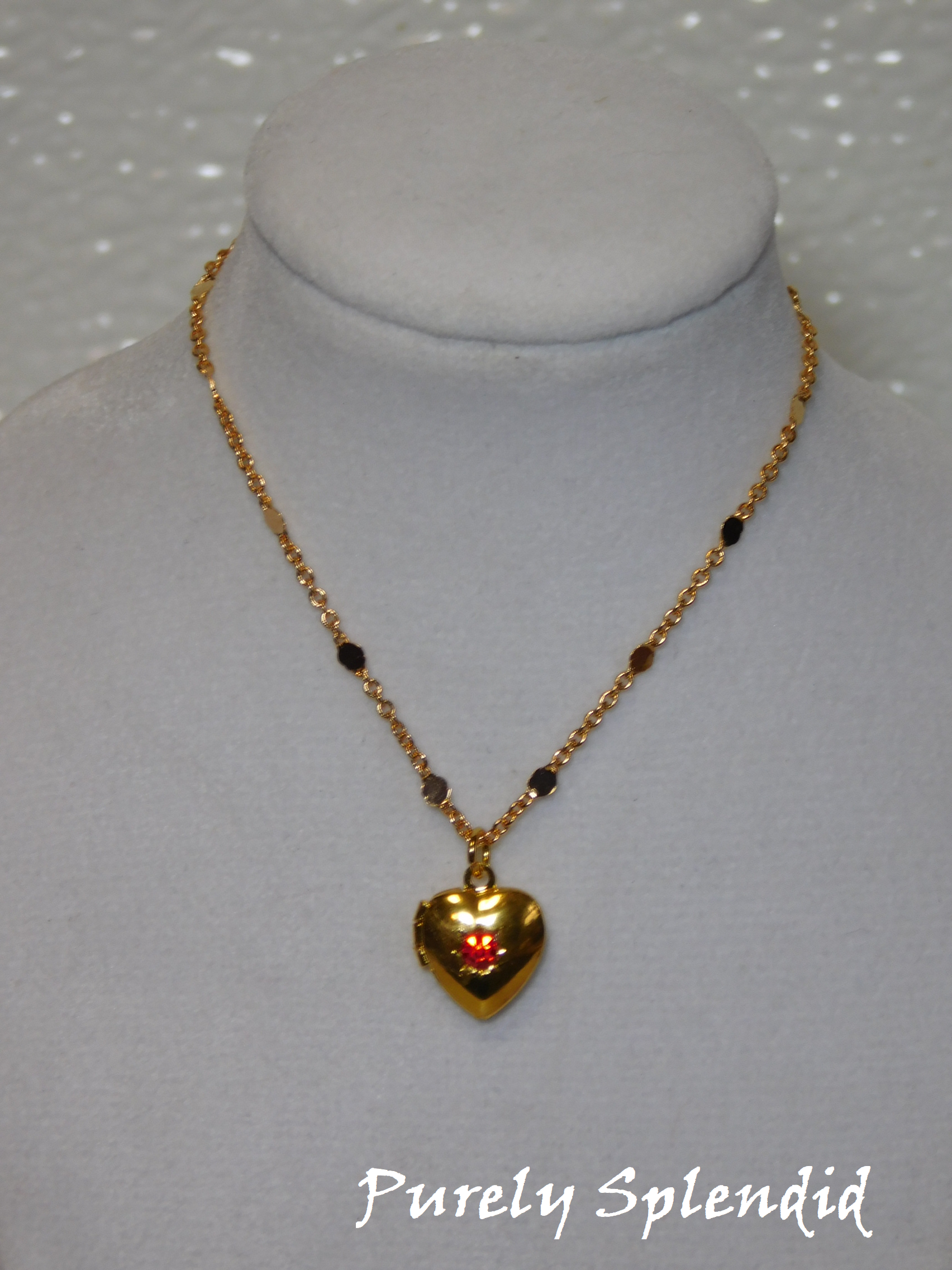 gold heart locket with a red center crystal hanging on a pretty gold chain