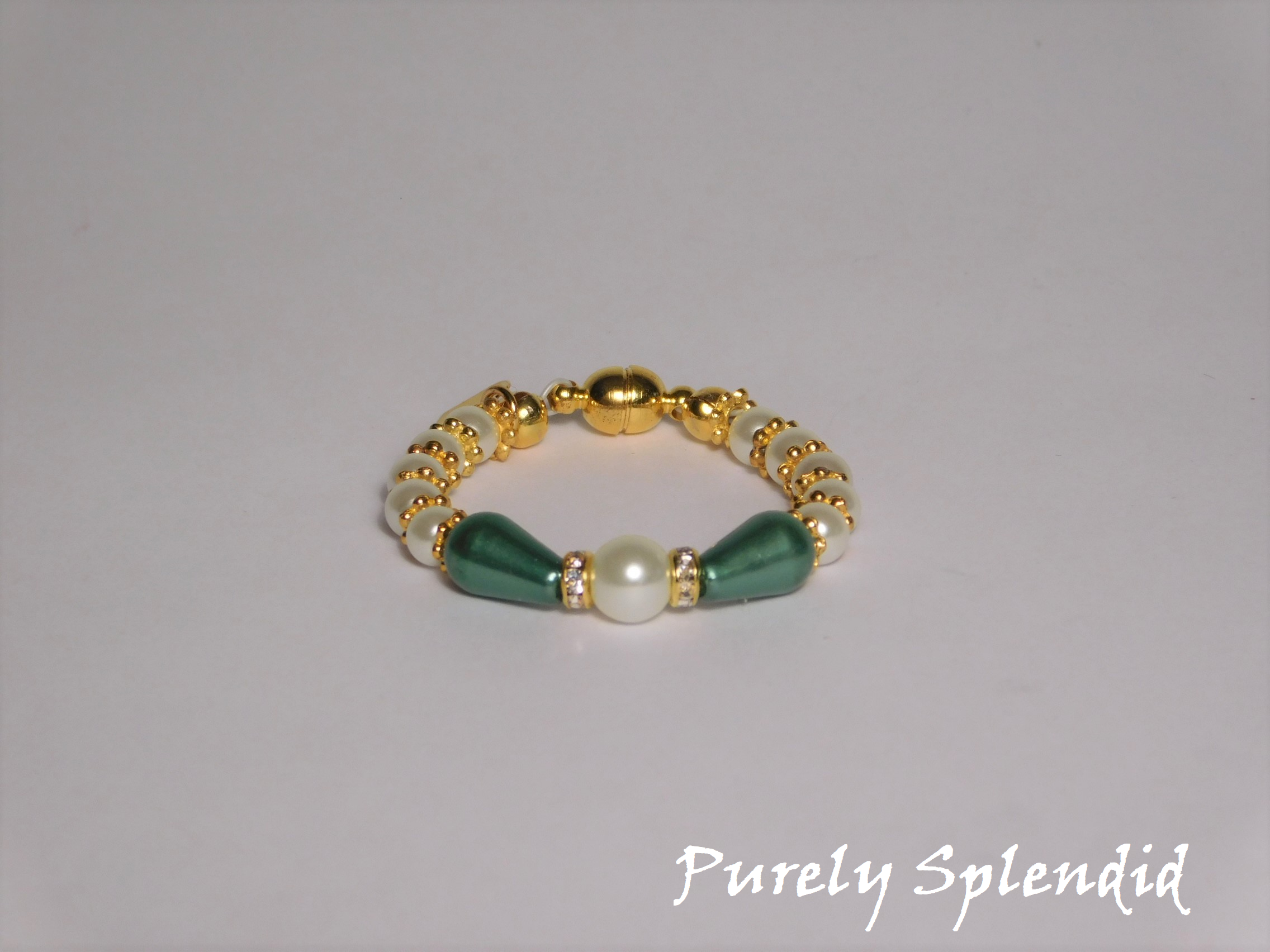 round white pearls with gold spacer beads with the main focus made up of one large white pearl bead surrounded by a thin sparkling bead and green pear shaped pearl 