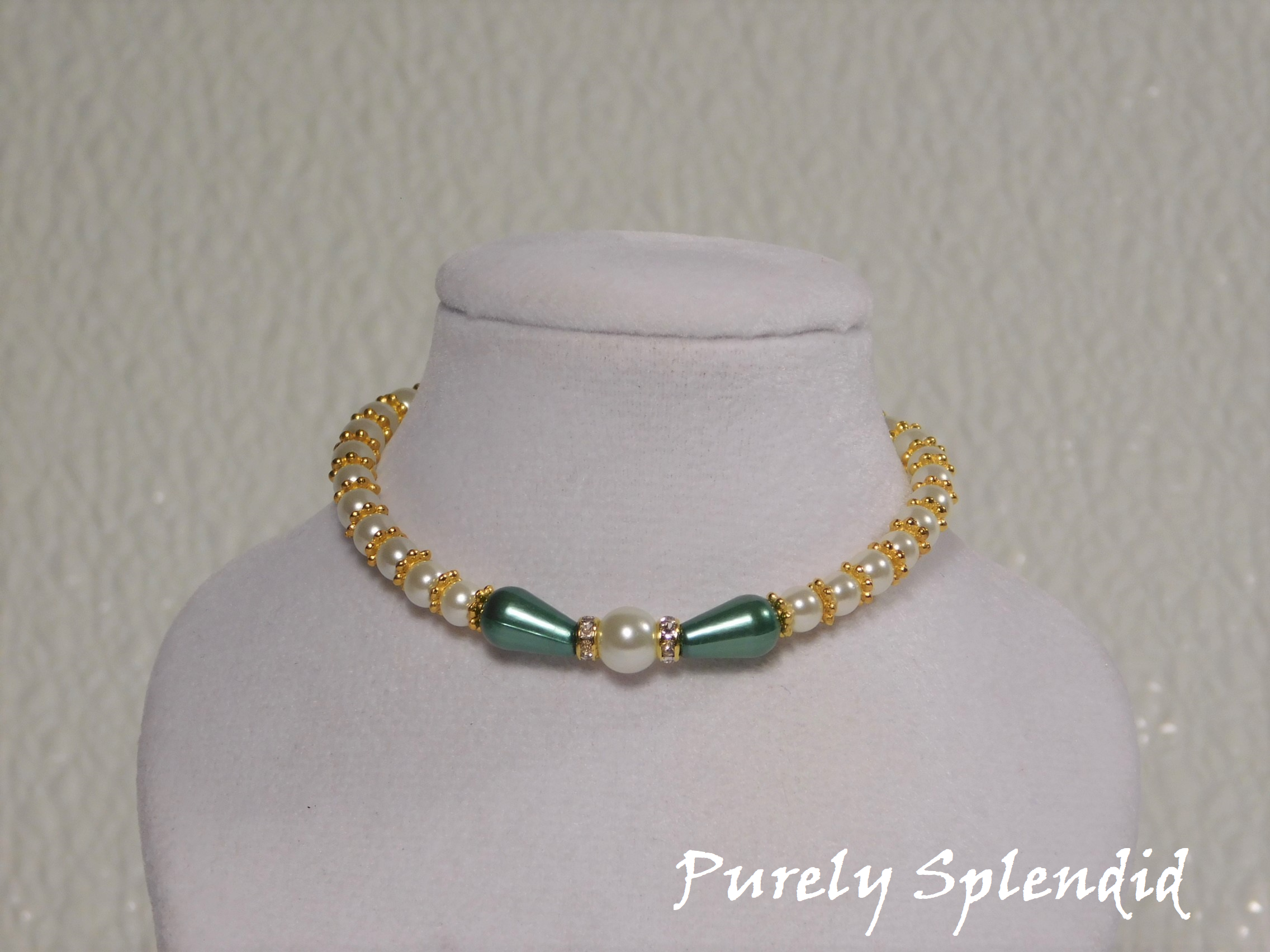 one large round white pearl surrounded by a thin sparkling bead and green pear shaped pearl bead. The rest of the necklace is made up with round white pearls alternating with gold spacer beads