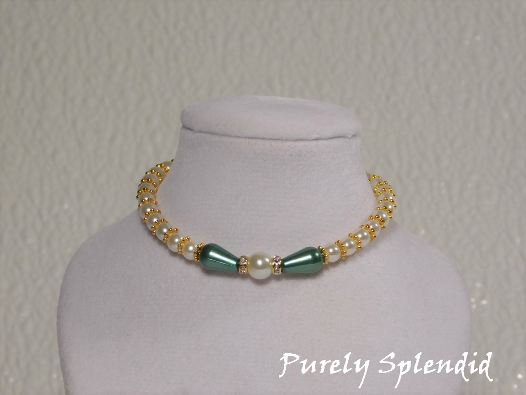 one large round white pearl surrounded by a thin sparkling bead and green pear shaped pearl bead. The rest of the necklace is made up with round white pearls alternating with gold spacer beads