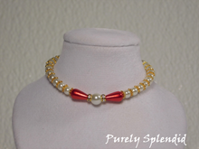 Load image into Gallery viewer, one large round white pearl surrounded by a thin sparkling bead and red pear shaped pearl bead. The rest of the necklace is made up with round white pearls alternating with gold spacer beads
