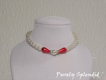 Load image into Gallery viewer, one large round white pearl surrounded by a thin sparkling bead and red pear shaped pearl bead. The rest of the necklace is made up with round white pearls alternating with silver spacer beads

