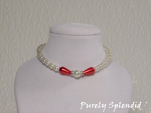 one large round white pearl surrounded by a thin sparkling bead and red pear shaped pearl bead. The rest of the necklace is made up with round white pearls alternating with silver spacer beads