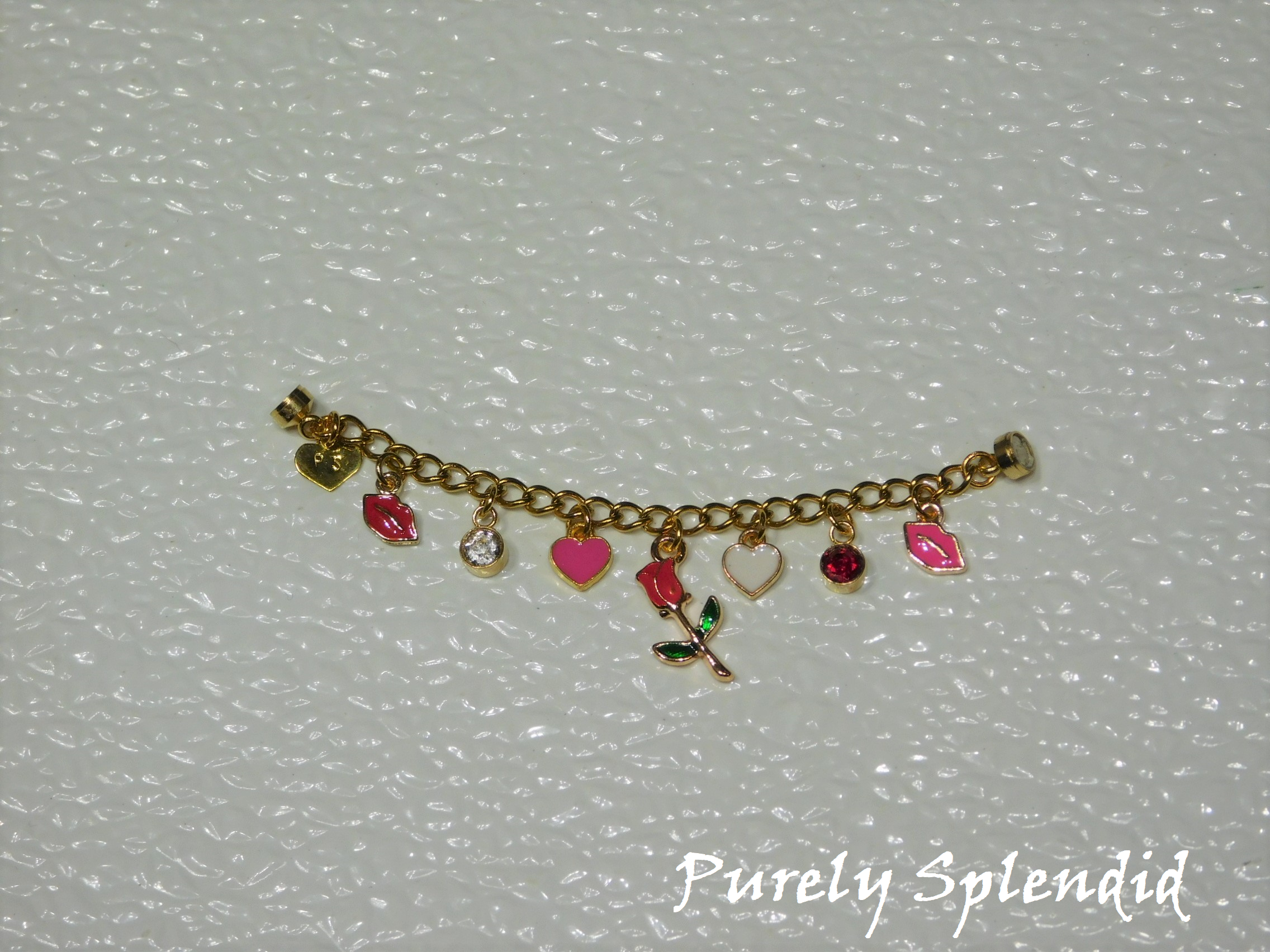 seven charms on a gold chain. red lips, crystal, pink heart, red rose on a stem, white heart, red crystal and pink lips.
