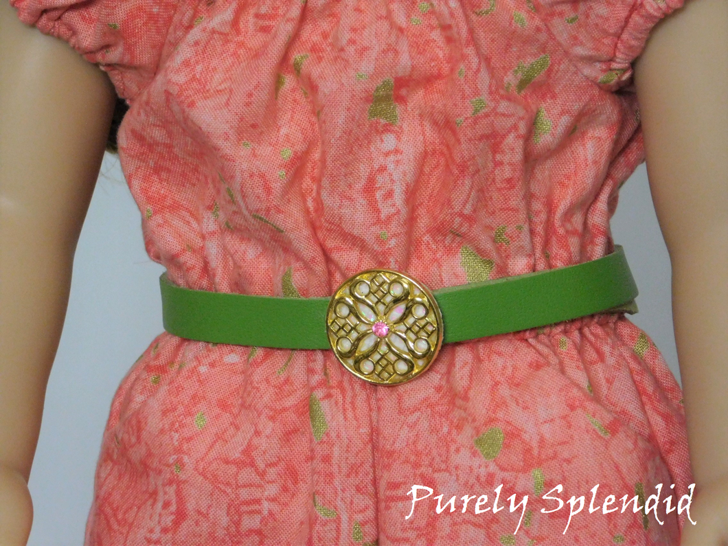 Green belt approximately 1/2 inch wide with a flat round ornamental gold buckle that has a light pink center crystal shown on an 18 inch doll