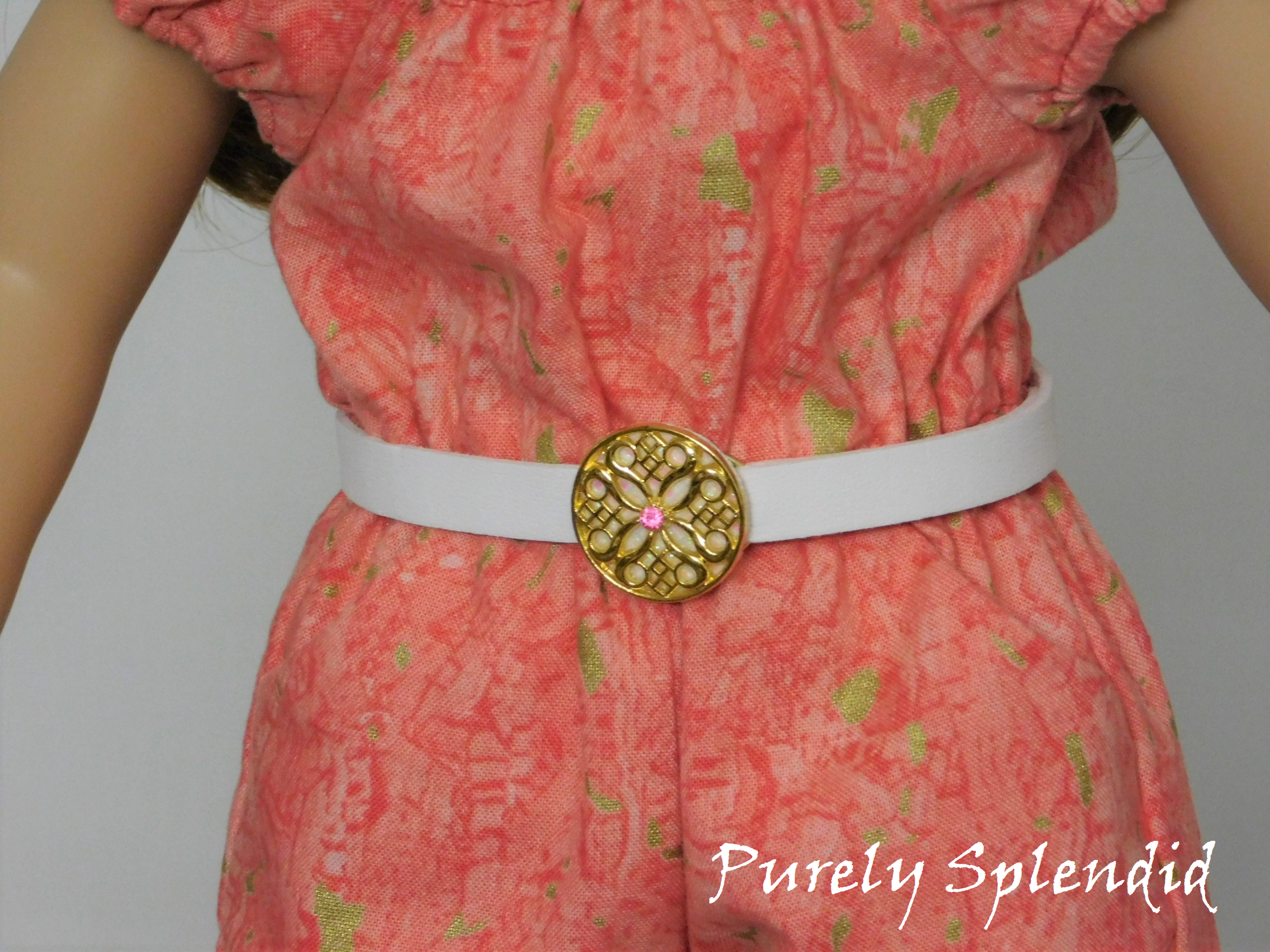 White belt approximately 1/2 inch wide with a large flat gold ornamental buckle which has a light pink center crystal shown on an 18 inch doll