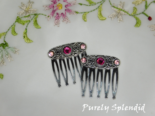silver colored 1 inch hair combs with silver colored decorative focal point. A pair of light pink super sparkling crystals are on the edges with a larger super sparkling magenta crystal in the center. Set of two combs