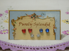 Load image into Gallery viewer, Red Hearts, Round Blue Catseye studs and a pair of Silver Star Studs shown on a presentation card

