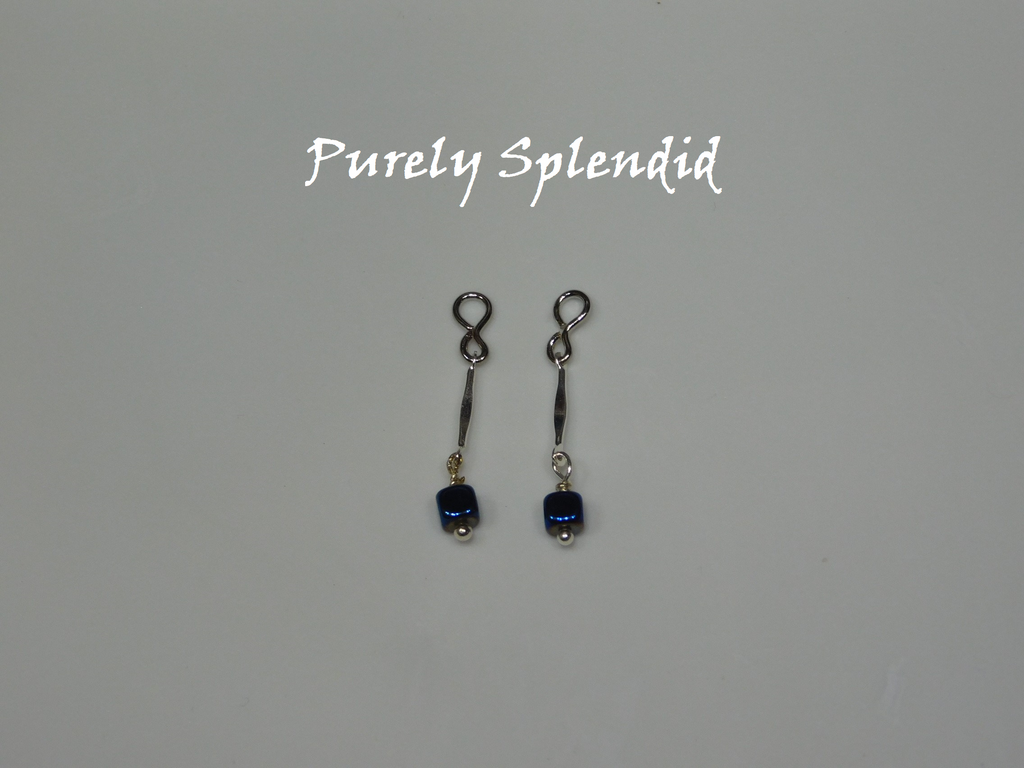Long thin silver bead with a dark blue square bead dangling below. Shown on a white background